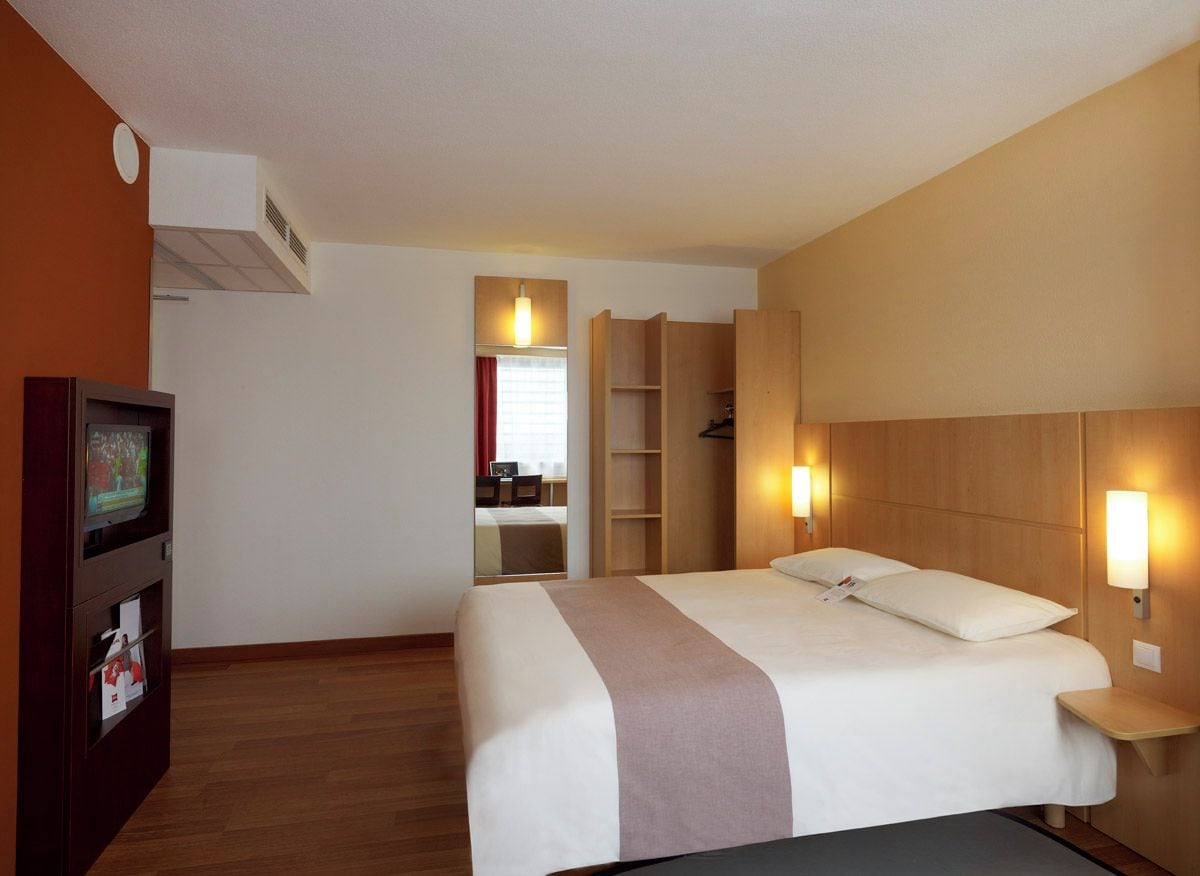 A hotel room with a bed, a TV, a wardrobe, and a desk.