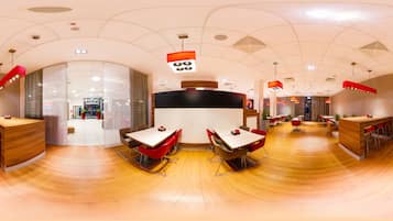 Un restaurante moderno con suelo de madera curvada, sillas rojas y marrones, y una mesa central.