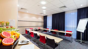 Ein Konferenzraum mit langen Tischen, roten Stühlen, einer Whiteboard und einer Obstauslage.