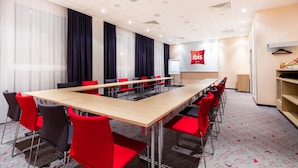 Una sala de conferencias con una larga mesa, sillas rojas y negras, una pizarra y un perchero.