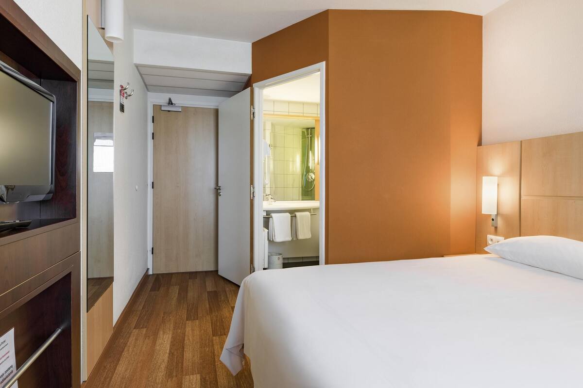 A hotel room with a bed, a television, a bathroom with a mirror, and a door leading to another room.