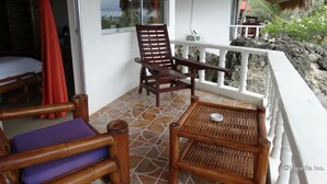 Une chaise et une table en bois sur un balcon, avec vue sur l’océan et un toit de chaume.