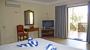 Une chambre d’hôtel comprenant un lit, un bureau avec une chaise, une télévision et un balcon avec des rideaux.