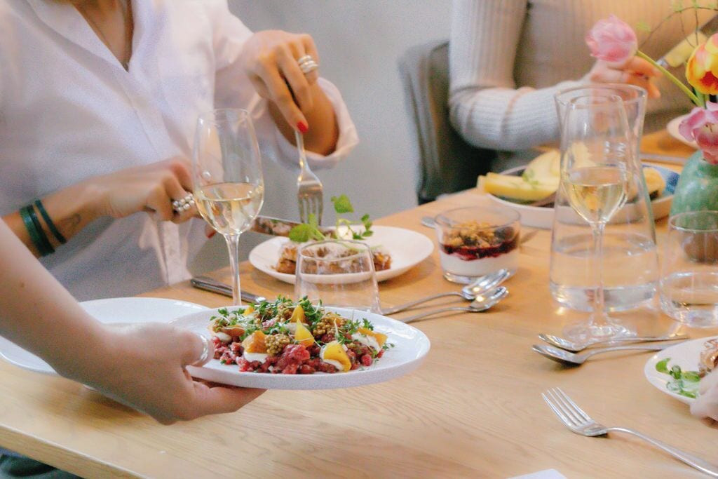 A dining table with plates of food, wine glasses, and cutlery.