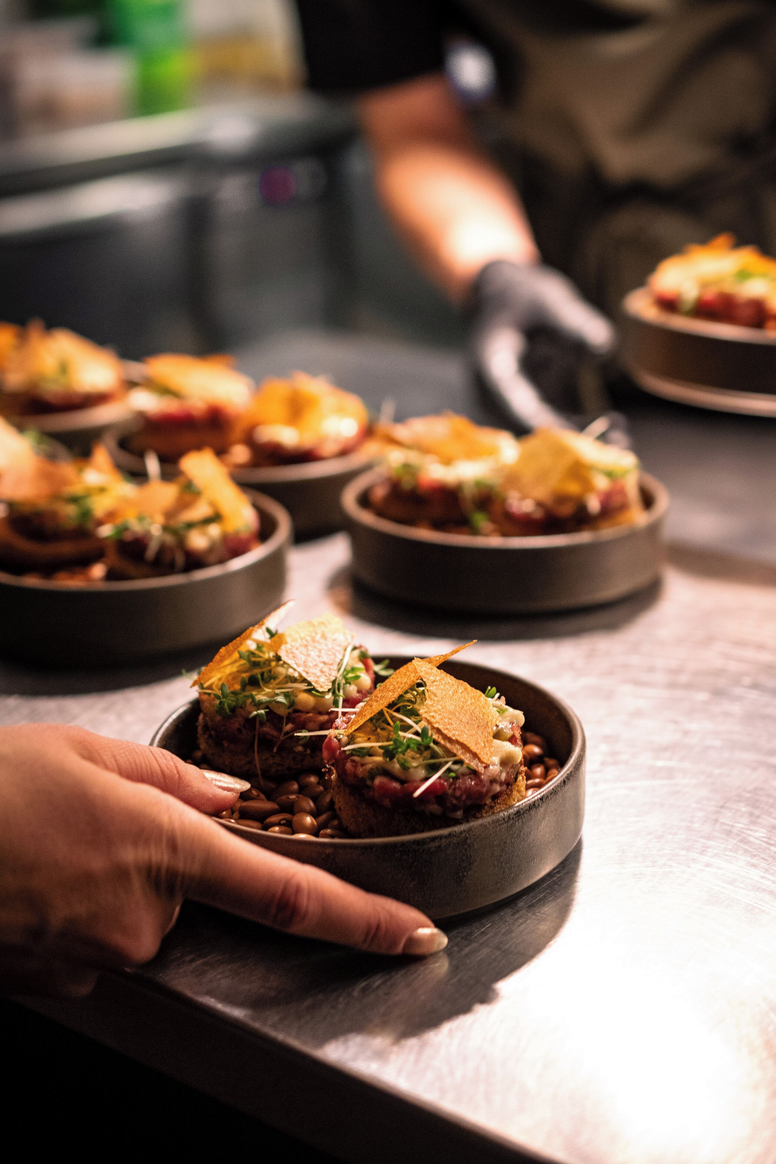 A chef's hand holding a bowl of food with a garnish on top.