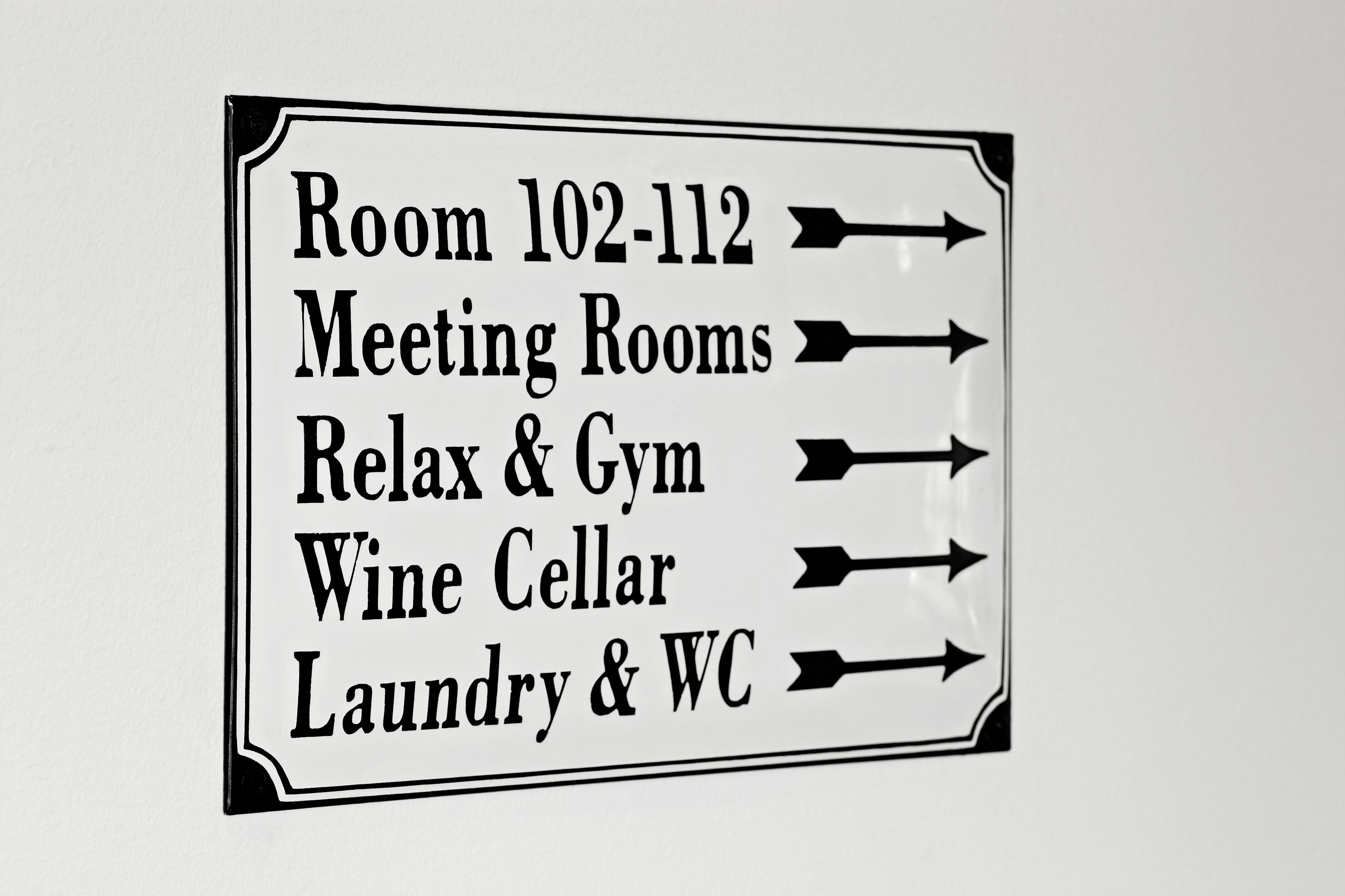 Placa indicativa com setas apontando para diversos serviços do hotel, incluindo salas de reunião, área de relaxamento e academia, adega de vinhos e lavanderia e sanitários.