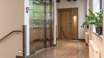 Un couloir avec un ascenseur moderne, un escalier doté d’une rampe et une plante en pot.