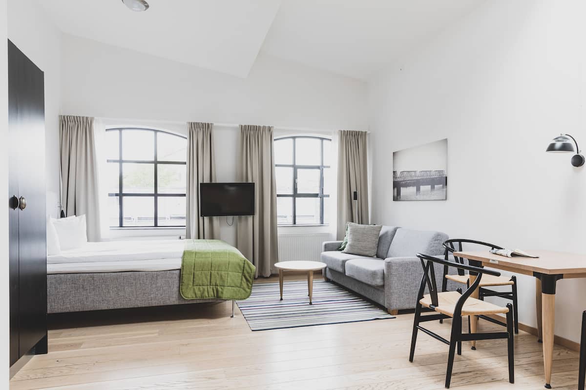 A modern living room with a bed, sofa, TV, and dining area.