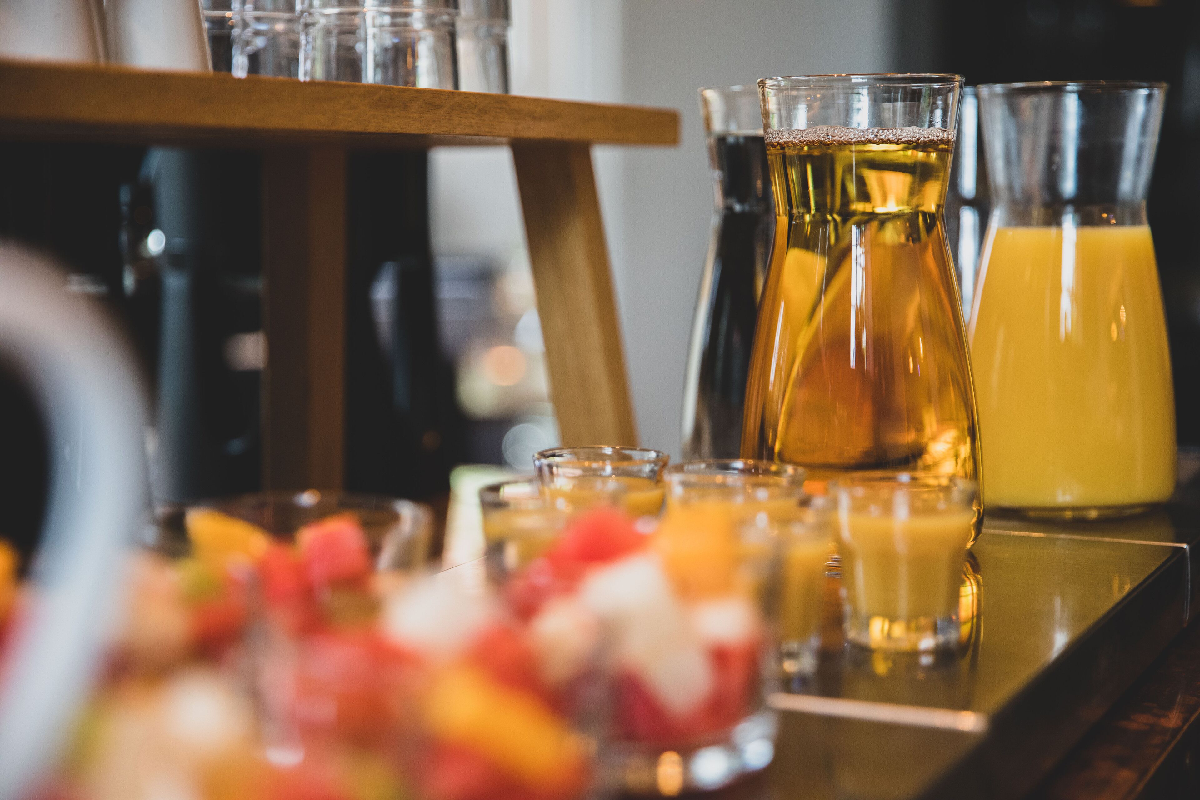 A bar area with various glasses and bottles of beverages, a wooden shelf, and a fruit bowl.
