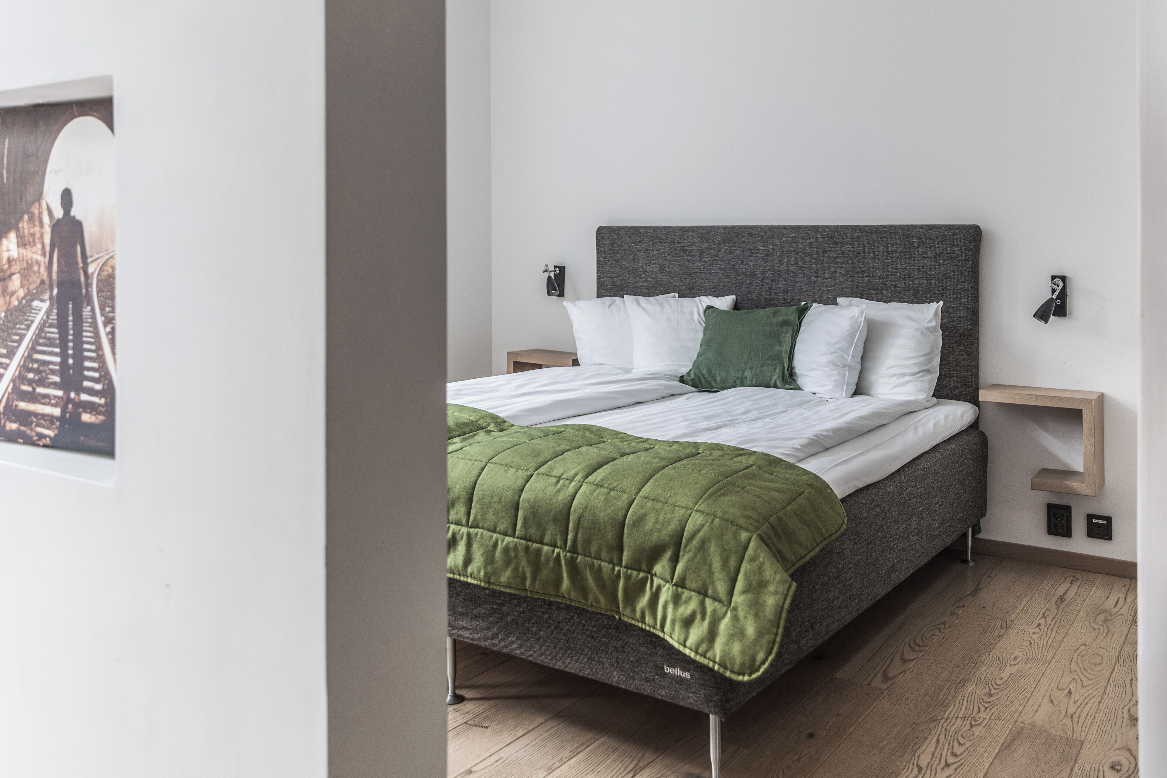 Un dormitorio moderno con cama, ropa de cama verde y blanca, cabecera gris y suelo de madera.