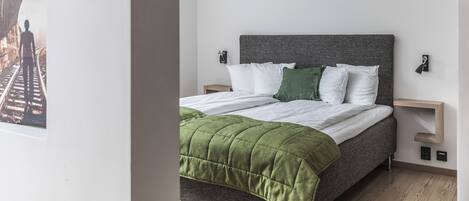 Un dormitorio moderno con cama, ropa de cama verde y blanca, cabecera gris y suelo de madera.
