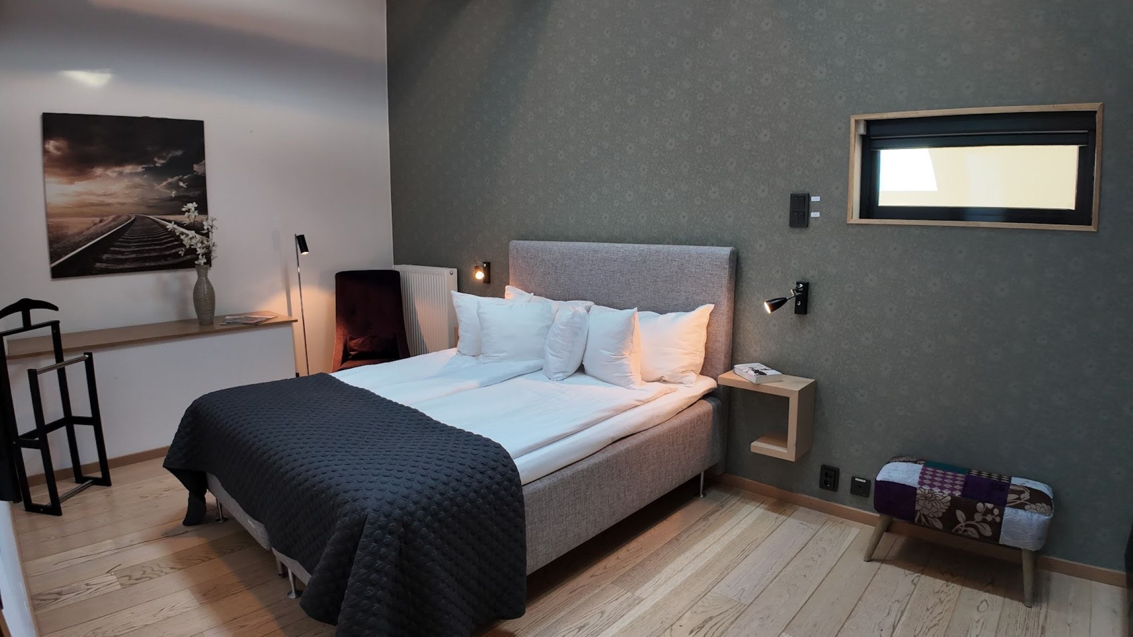 Un dormitorio moderno con una cama grande, una mesita de noche, un televisor montado en la pared y un cuadro.