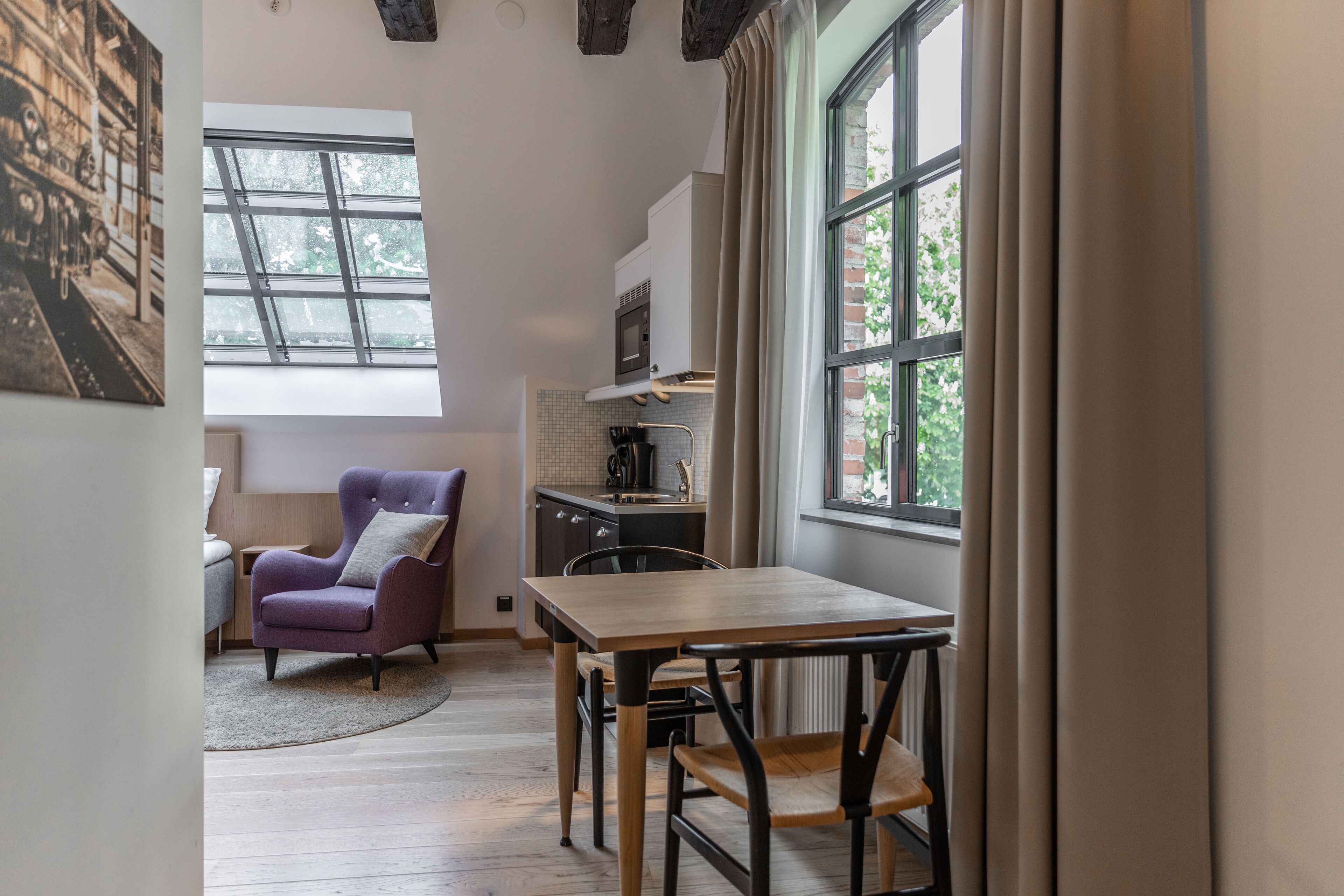 A modern kitchen with a large window, a dining table, and a purple armchair.