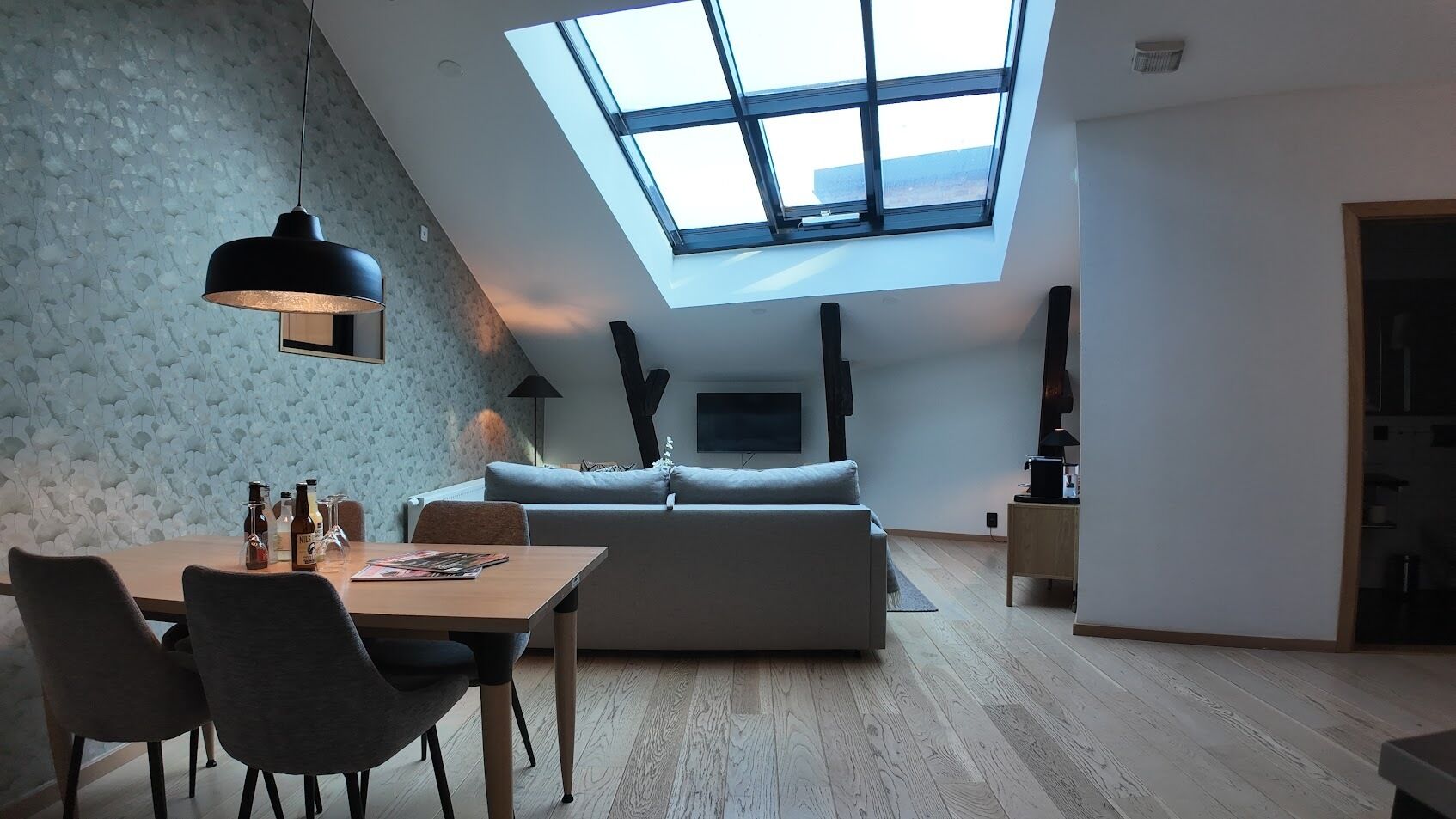 Un loft moderno con tragaluces, un comedor con sillas y botellas, y un espacio de sala acogedor con un sofá.