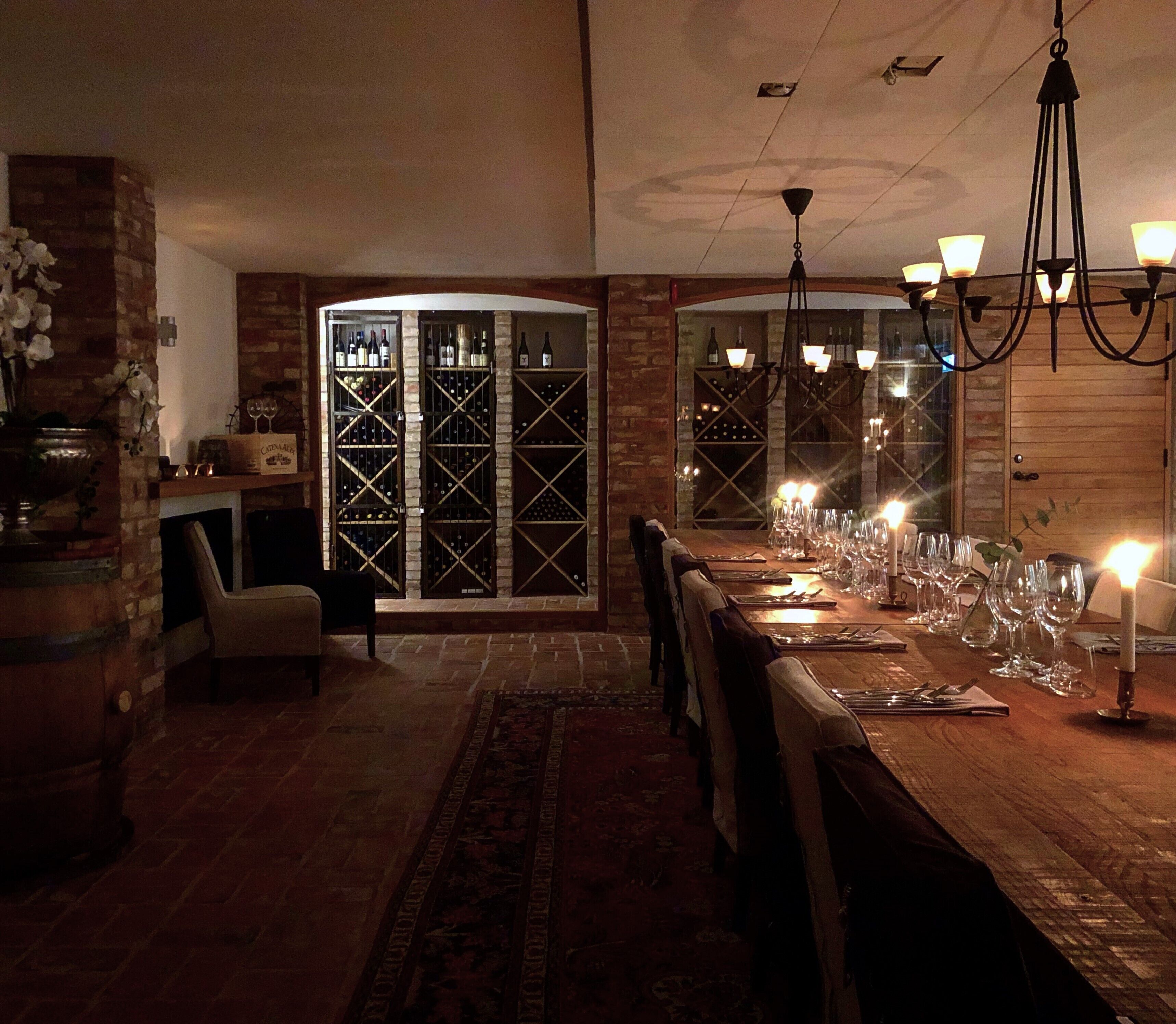 Ein Essbereich mit einem langen Holztisch, gedeckt für eine Mahlzeit, neben Weinregalen und einer Backsteinwand.