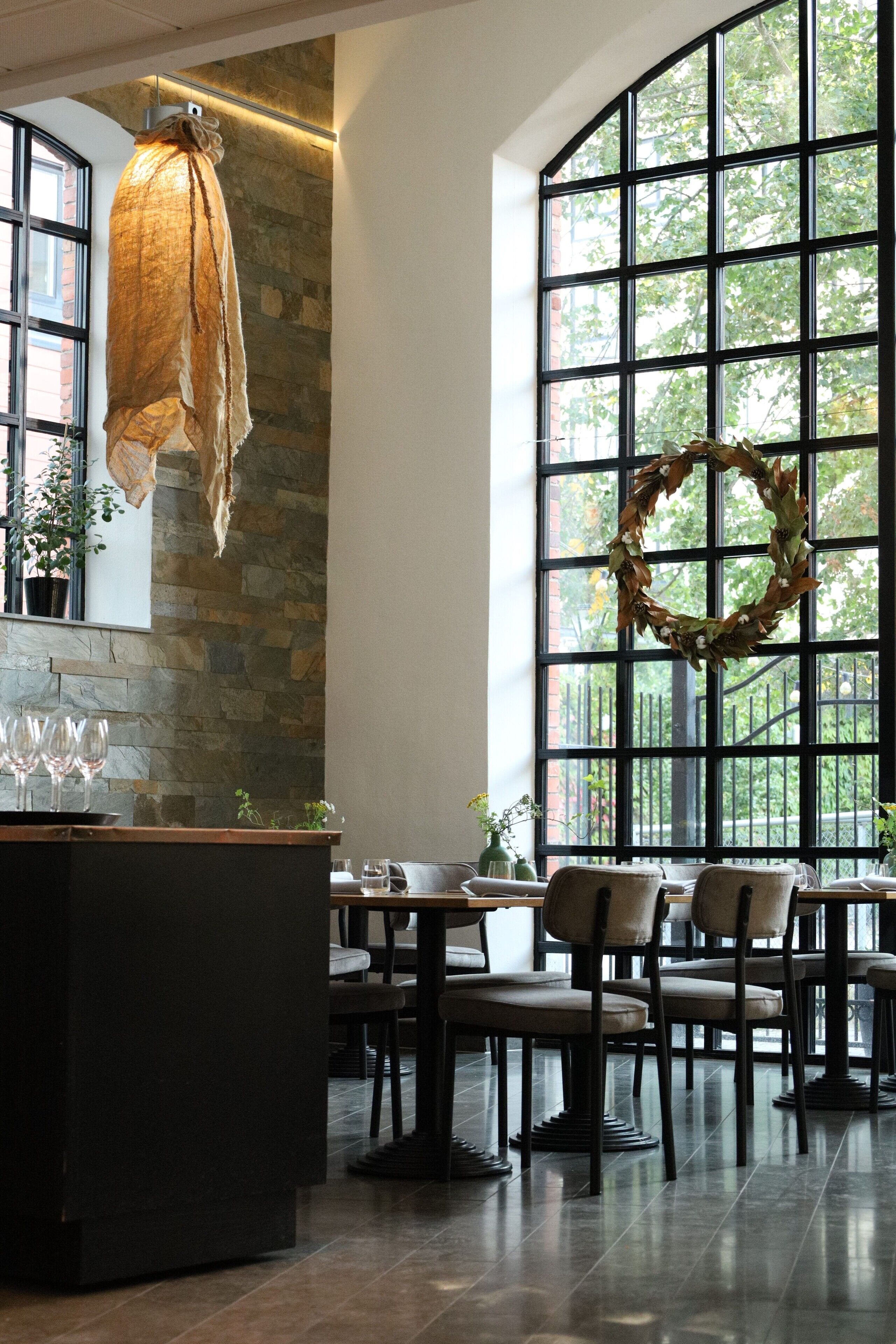 A restaurant with stone walls, large windows, and a central seating area with tables and chairs.