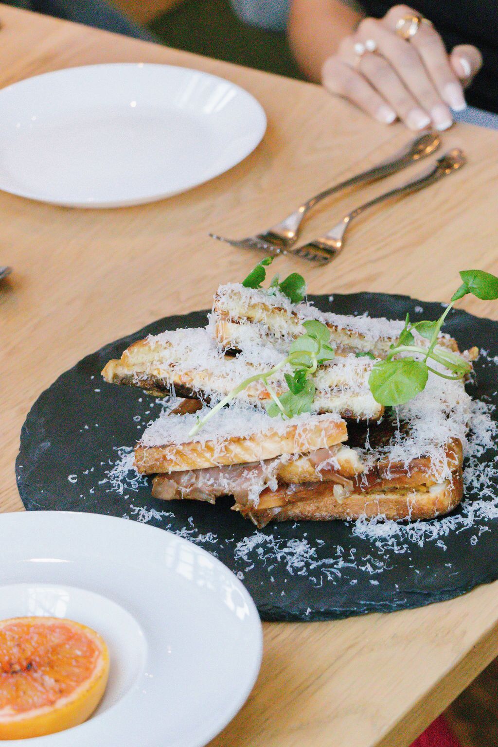 Un plato de comida con una rebanada de pan cubierta de queso y verduras, media limón y un plato negro.