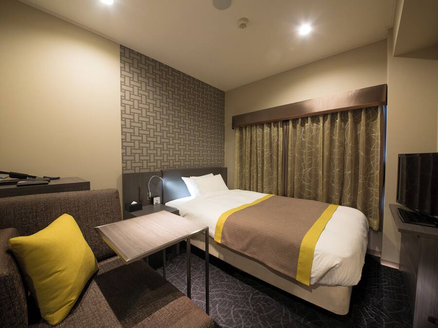 A hotel room with a bed, a desk, a chair, a TV, and a window with curtains.