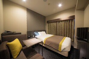 Habitación de hotel con cama, sofá, una mesita, televisor y una pared con diseño geométrico.