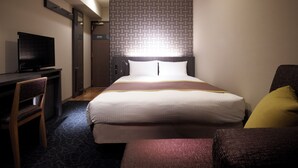 A hotel room with a bed, a desk with a television, a chair, and a patterned wall. - Almont Inn Nihonbashi (Tokyo)