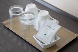 Una bandeja con un vaso, dos tazas y un bol que contiene bolsitas de té.