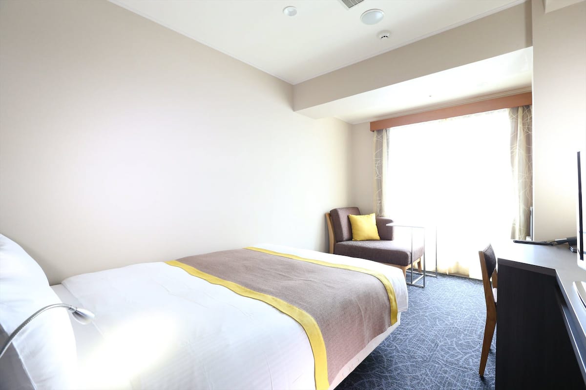 A hotel room with a bed, a desk, a chair, and a large window.