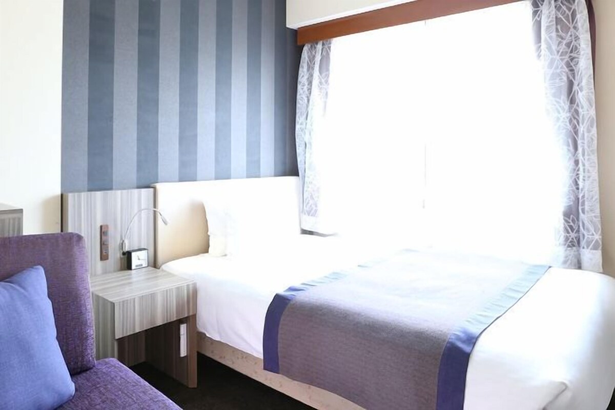 Une chambre d’hôtel avec un lit, une table de chevet, une lampe et une fenêtre avec des rideaux.