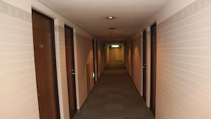 Un lungo e stretto corridoio di un hotel, con porte su entrambi i lati, pavimento in moquette e pareti di colore chiaro.