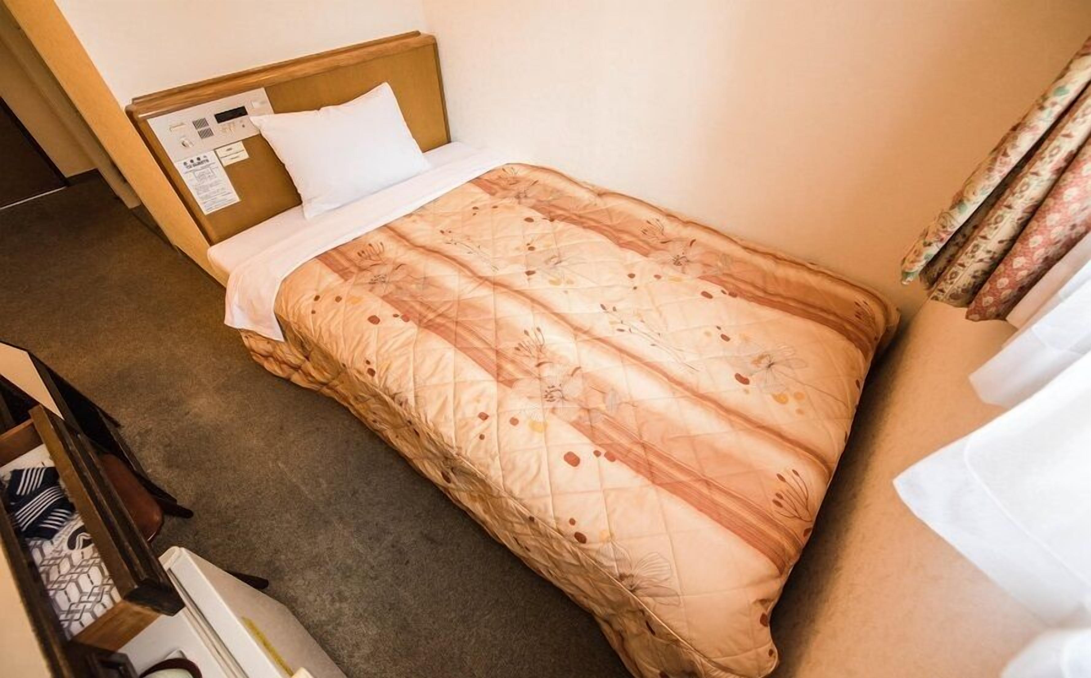 A single bed with a headboard, a white pillow, and a patterned bedspread.