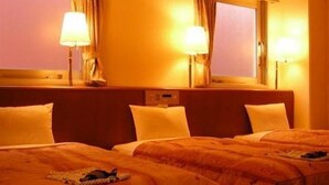 Una camera d'albergo con due letti, ognuno con copripiumino trapuntato e cuscini. Sono presenti due abat-jour e una finestra con tende.