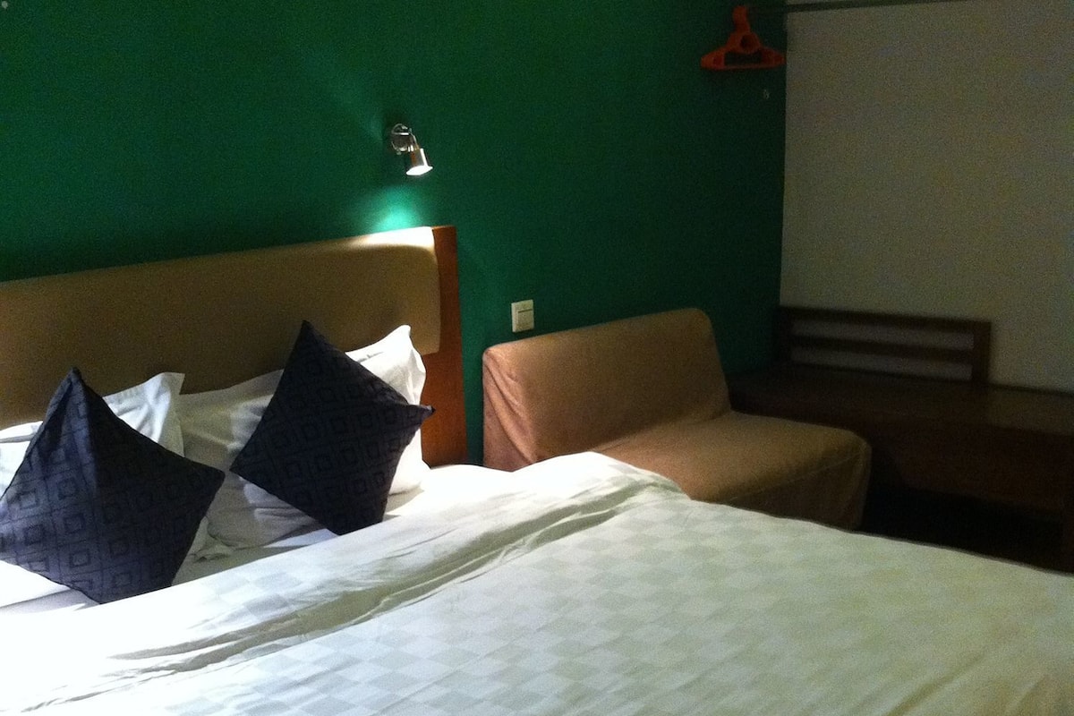 A hotel room with a bed, a chair, and a green wall.