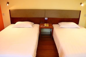 A hotel room with two single beds, a wooden headboard, a bedside telephone, and a wall-mounted light fixture.