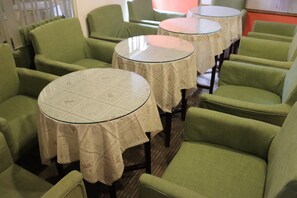 A room with multiple round tables covered with lace tablecloths and green upholstered chairs.