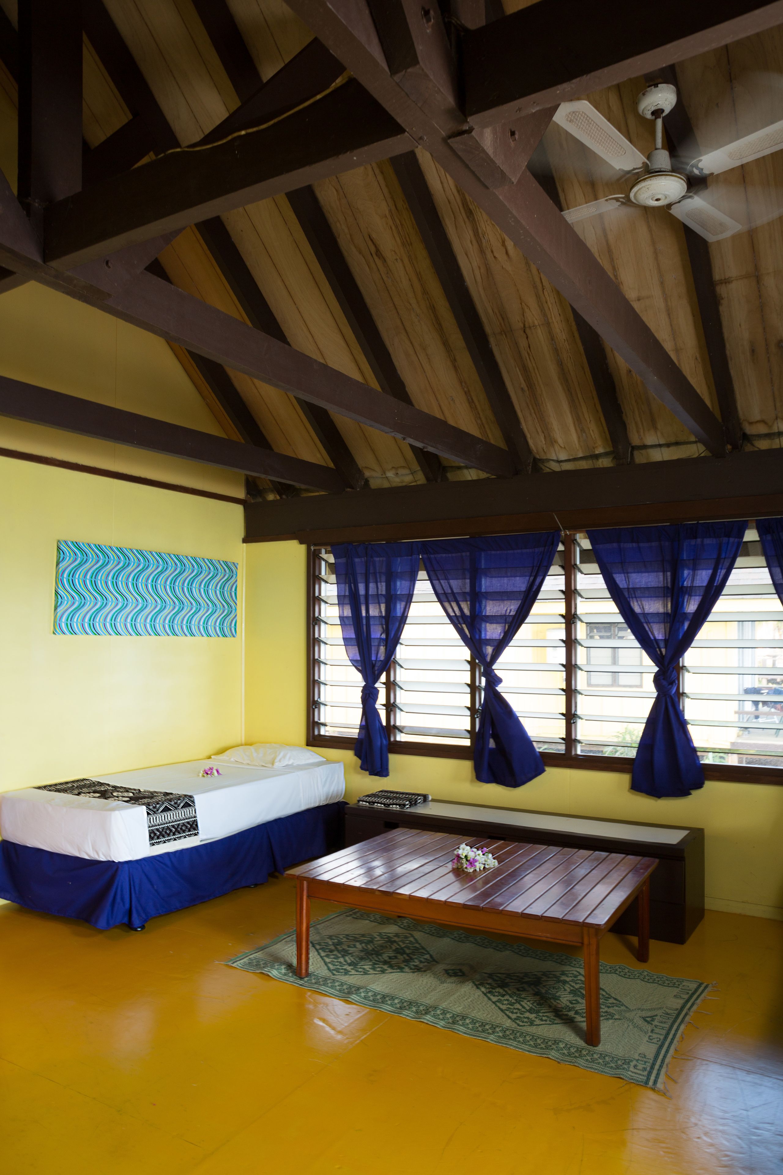 A room with a bed, a wooden table, and a ceiling fan.