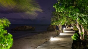 Un sentier en bois mène à une plage d’où l’on peut admirer l’océan et les rochers.