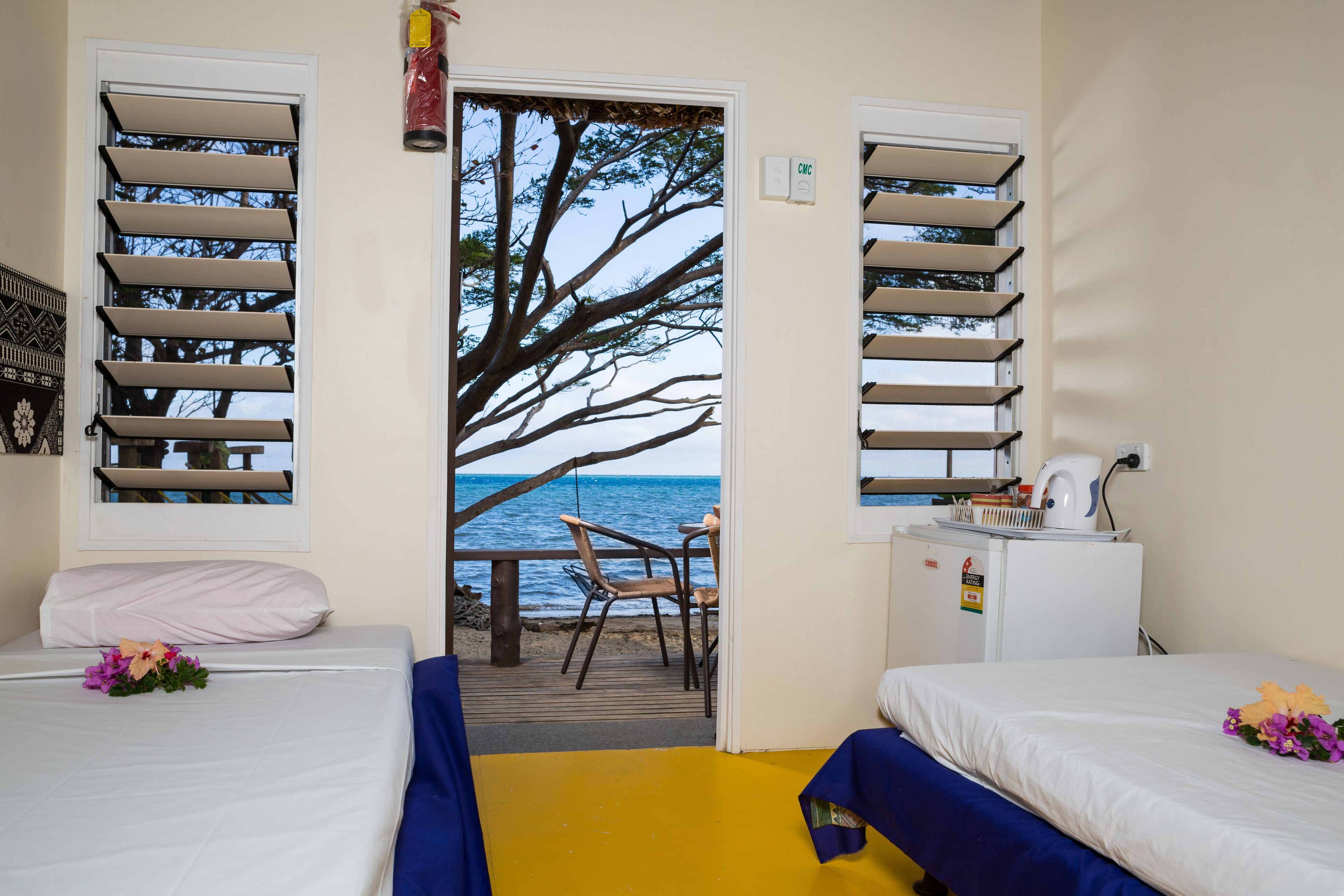 A room with two beds, a small table, and a chair near a window overlooking the sea.