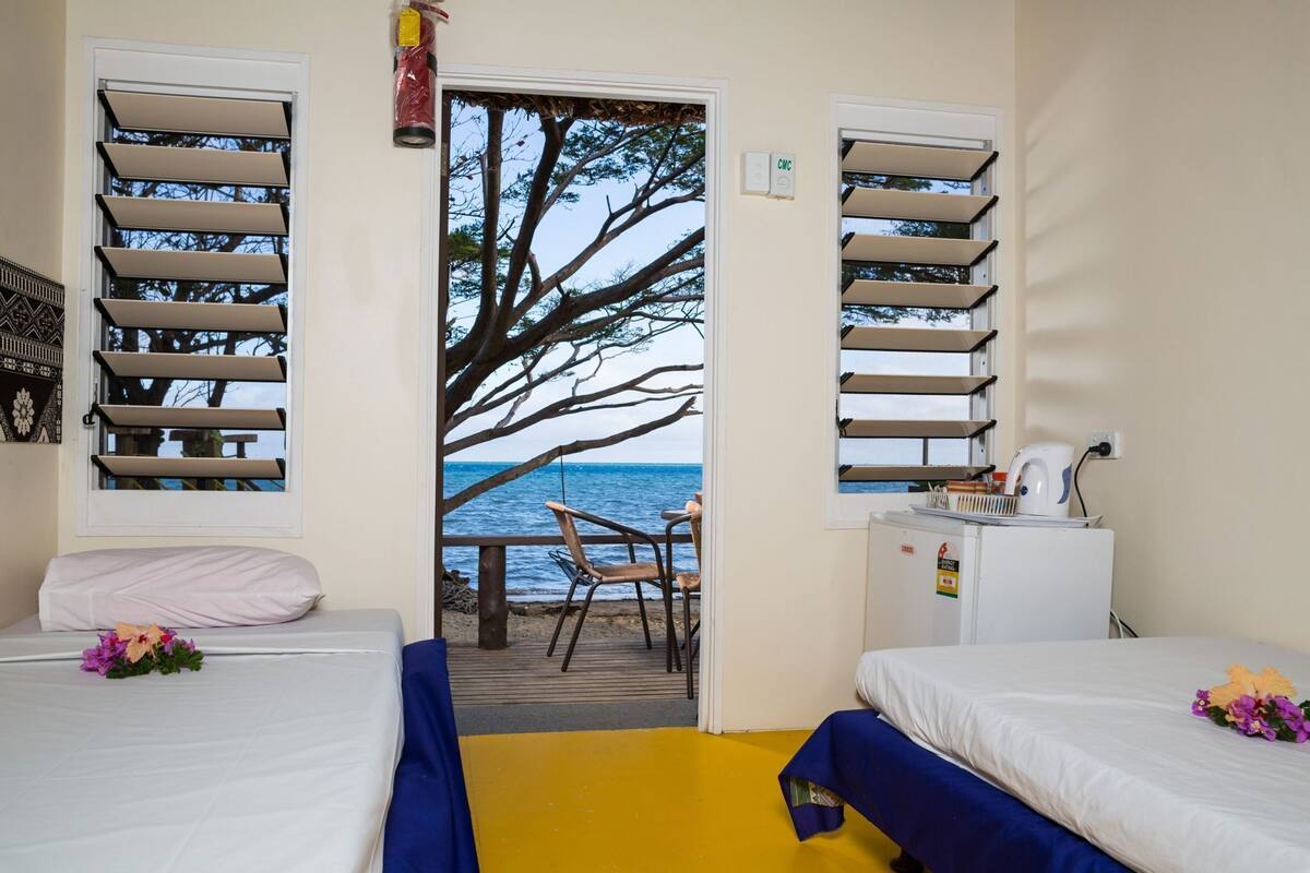 A room with two beds, a small table, a chair, and a view of the sea.