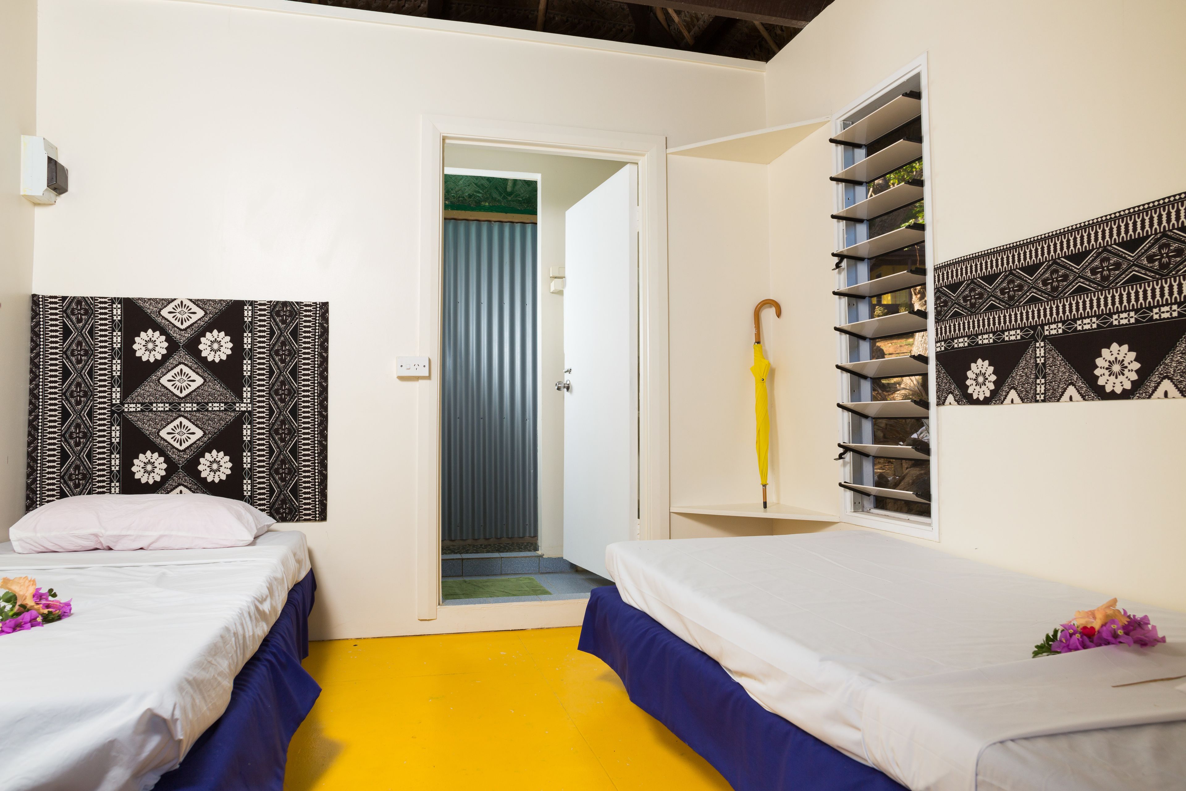 A room with two beds, a yellow floor, and patterned wall art.