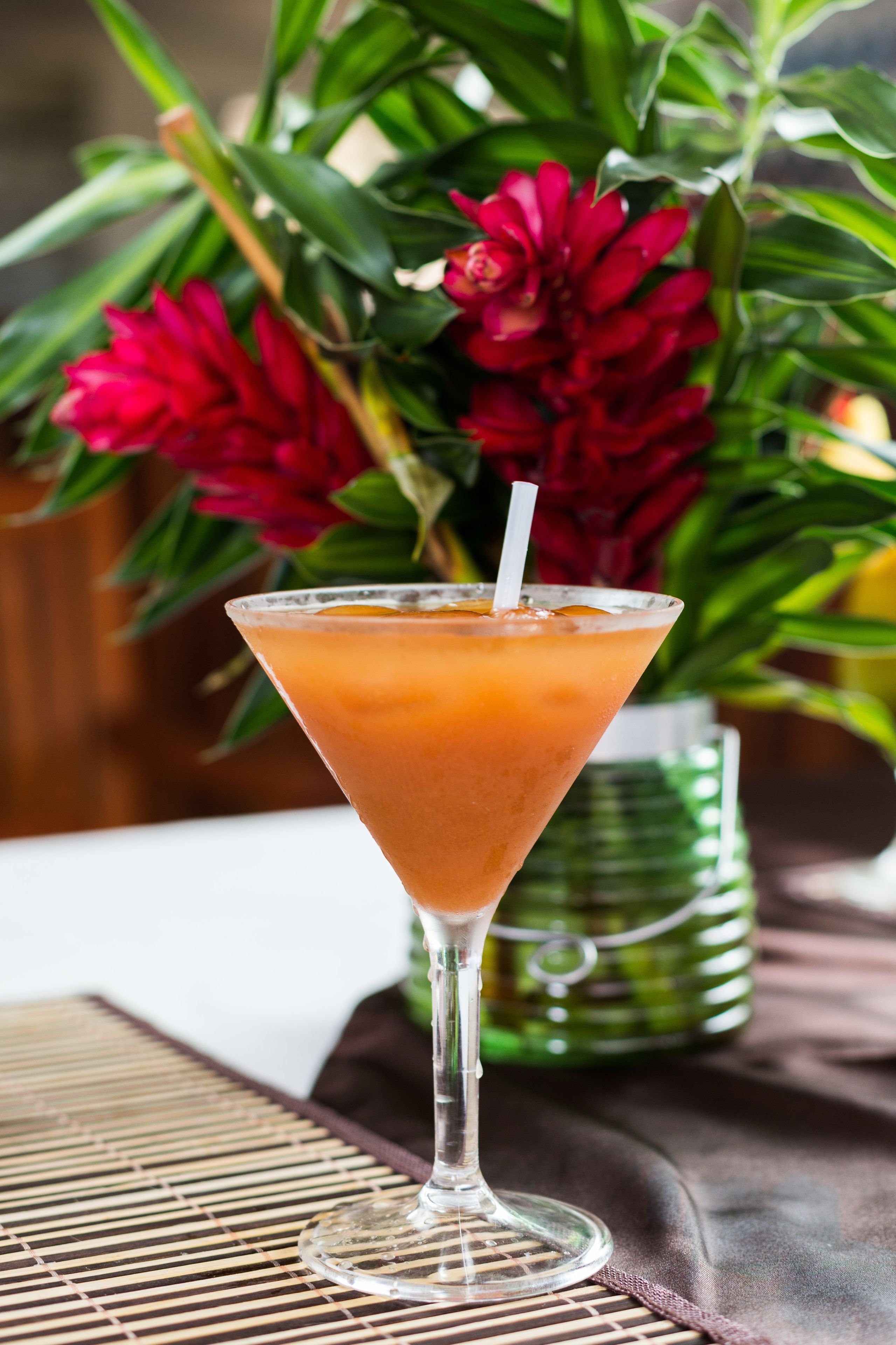 Una copa de martini con pajita sobre una estera de bambú.