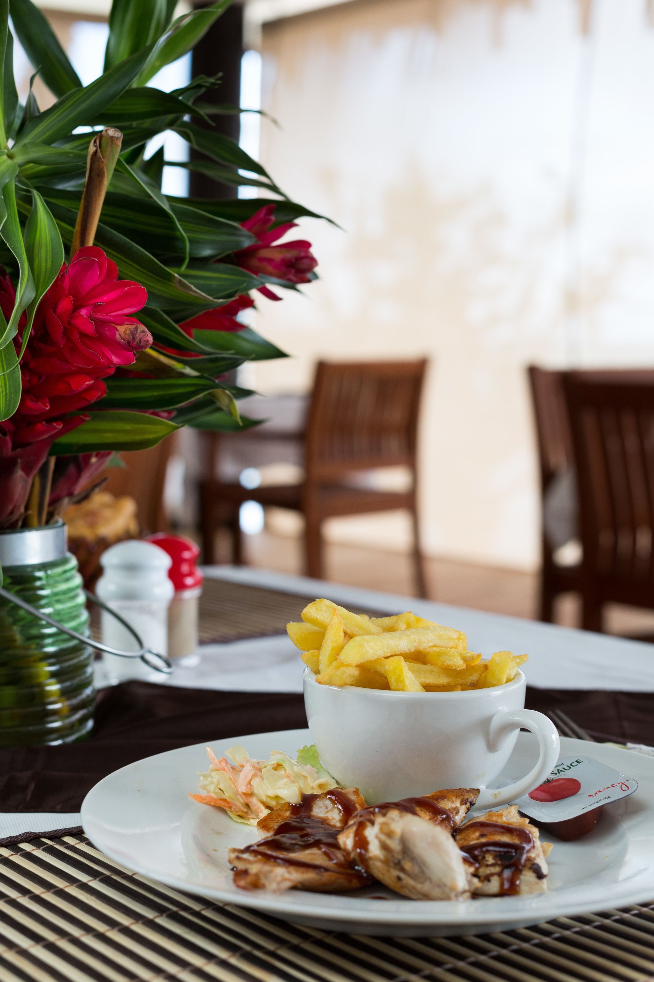 A dining table with a plate of food, a cup of fries, and a vase of flowers.