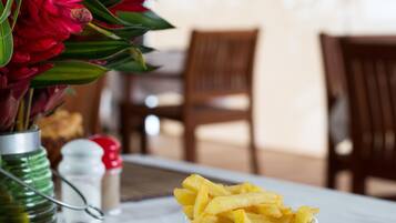 A dining table with a plate of food, a cup of fries, and a vase of flowers.