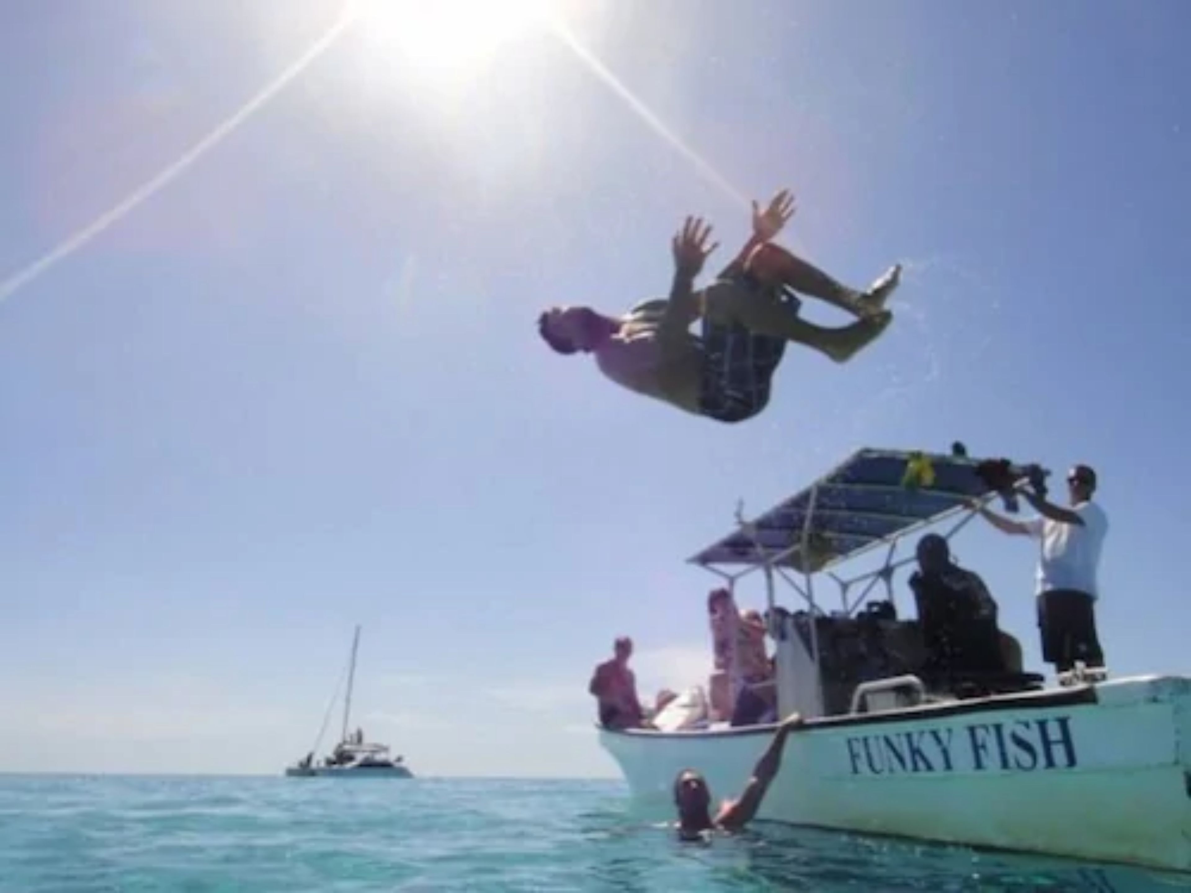 Iemand springt van een boot genaamd 'Funky Fish' in het water.