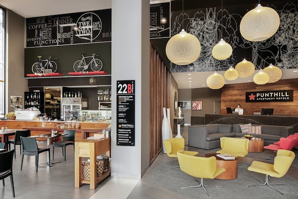 Un hall d’hôtel moderne comprenant un comptoir d’accueil, un espace salon et un bar à café.