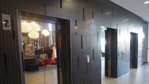 A modern lobby with a dark patterned wall, a seating area with red chairs, and a visible elevator. - Punthill Norwest (Norwest)