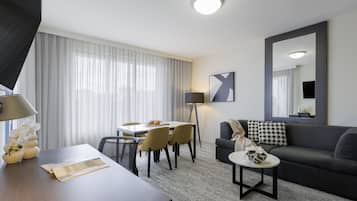 A modern hotel room with a dining area, a sofa, a coffee table, and a large mirror.