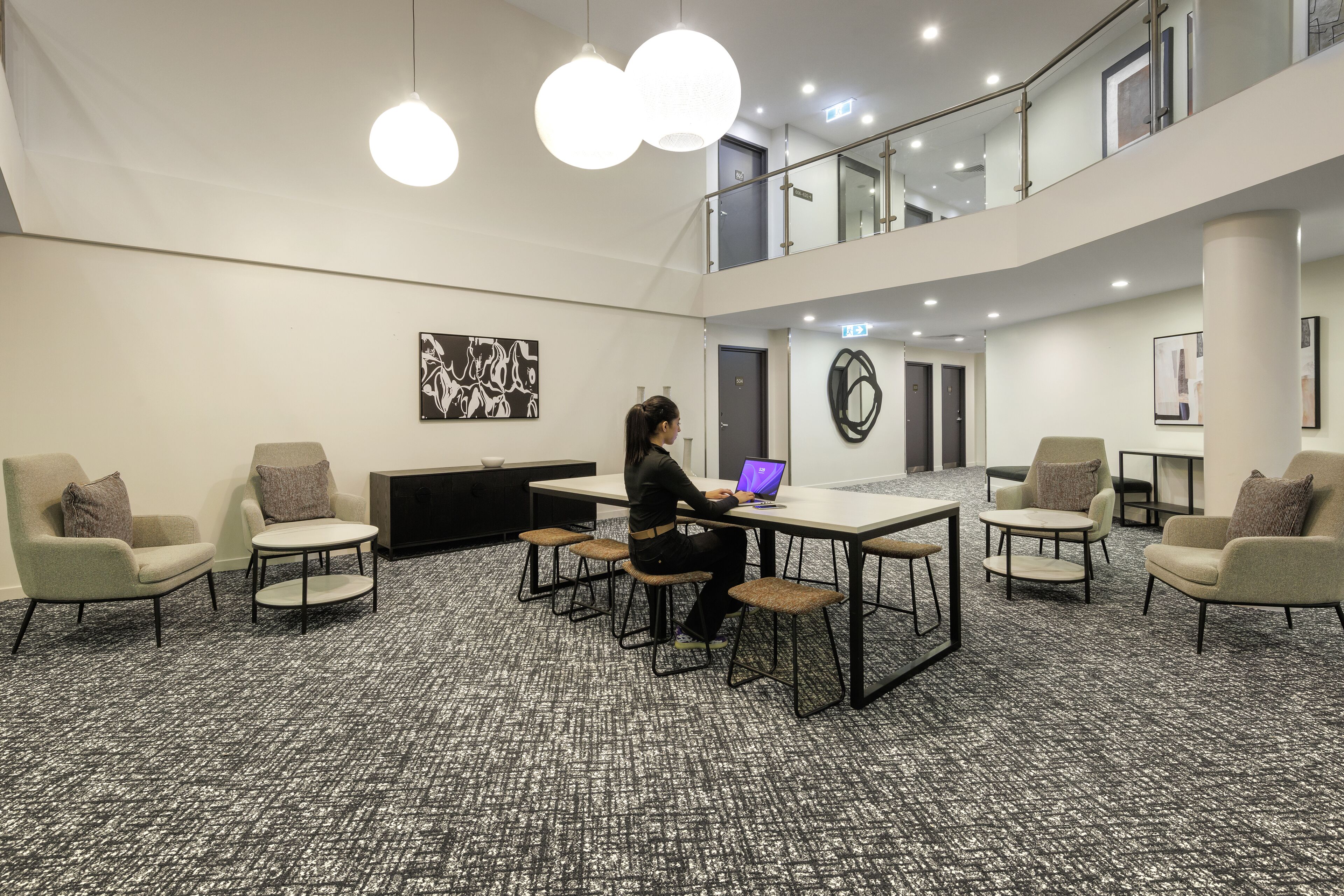 Une salle de conférence où une personne travaille sur un ordinateur portable, avec plusieurs chaises, des tables et un grand tableau abstrait accroché au mur.