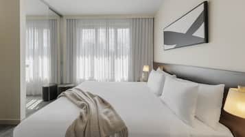 Ein modernes Hotelzimmer mit einem großen Bett, einem Nachttisch mit Lampe und Blick durch eine Glastür auf einen Balkon.