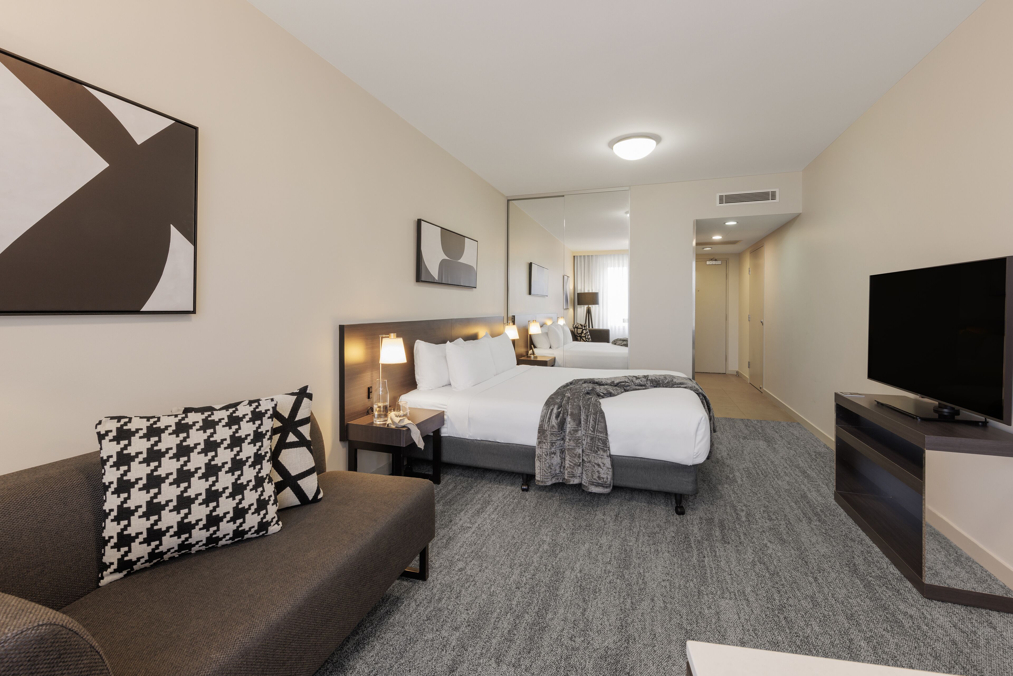 A hotel room with a bed, a sofa, a TV, and a large mirror.