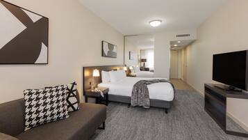 A hotel room with a bed, a sofa, a TV, and a large mirror.