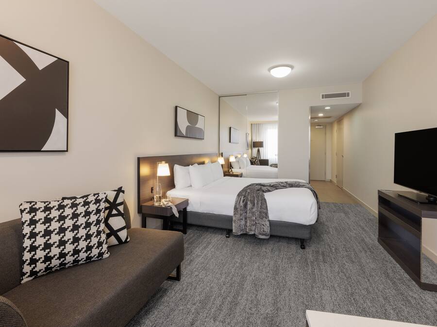 A hotel room with a bed, a sofa, a TV, and a large mirror.